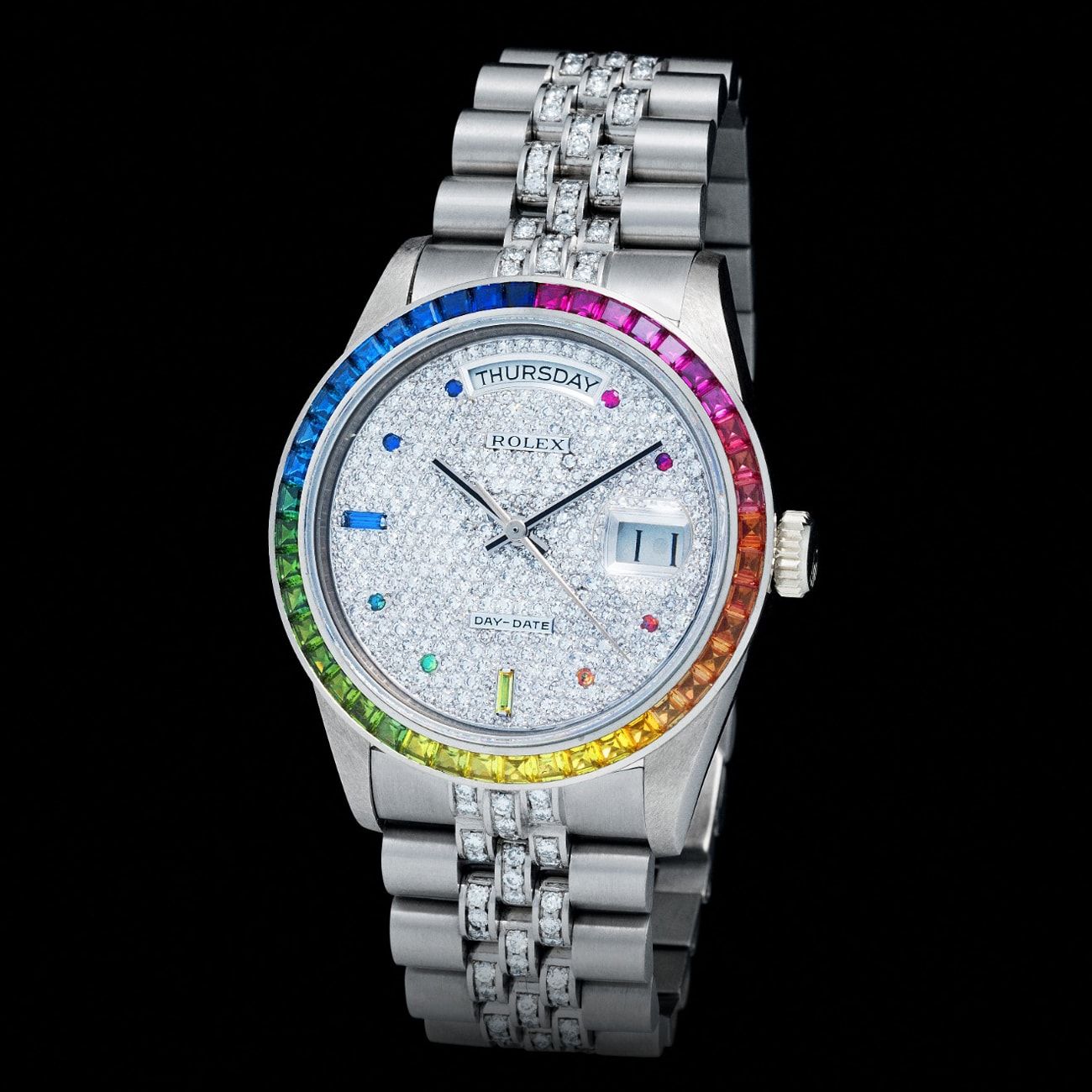 This incredibly stunning 1980s Rolex Day-Date reference 18 059 in 18k White Gold is from a batch of approximately only four Rolex Day-Dates, all in the same configuration, that were specially commissioned by his Majesty Qaboos bin Al Said, Sultan of Oman. The watches feature one of the earliest Rainbow Sapphire bezels paired with full diamond pave dial and bracelet. All four examples seen so far feature the Omani national emblem Khanjar on the case back and this particular example stands out for its red enameled finishing. This watch is certainly among the very rarest and most important Day-Date’s ever produced by the manufacturer.
